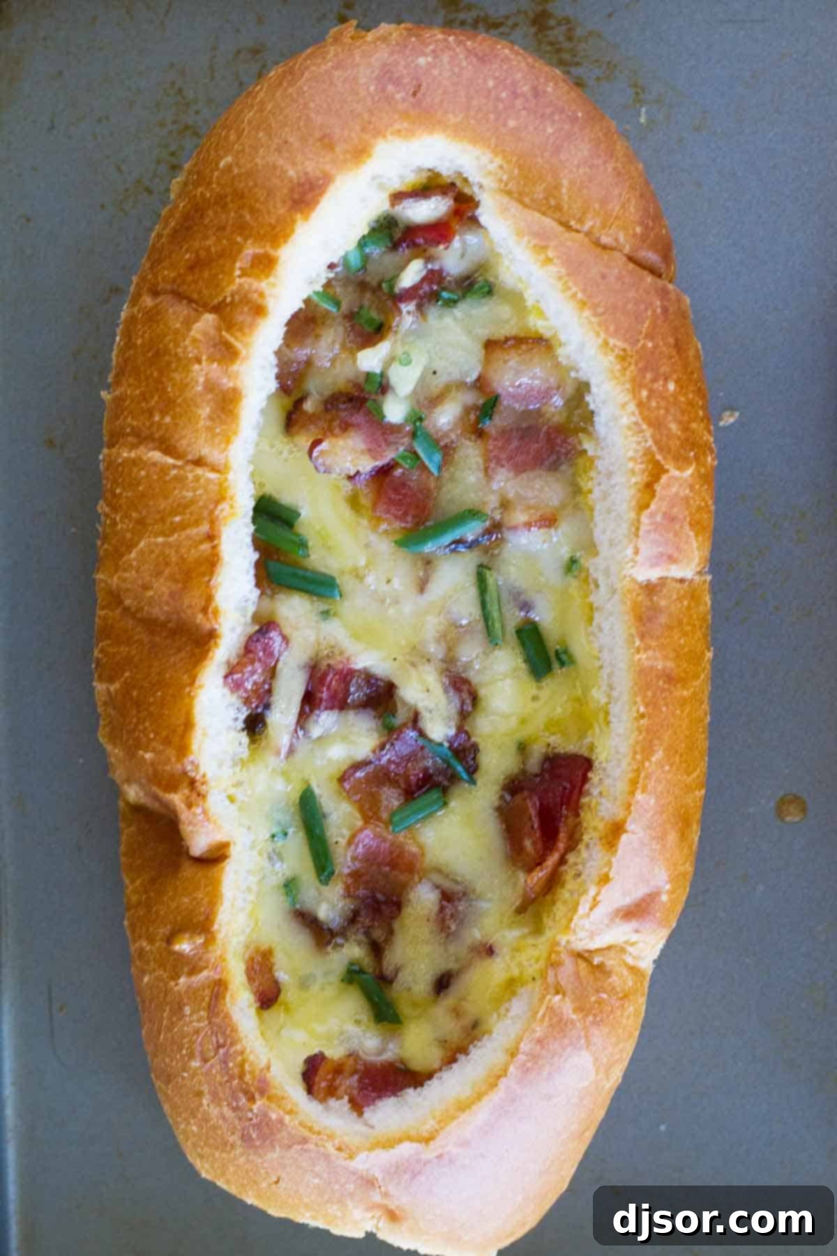 Ultimate Breakfast Bread Boats 3 A close-up shot of a submarine roll generously filled with baked eggs, crispy bacon, and melted cheese, showcasing the rich textures and appealing golden-brown top.