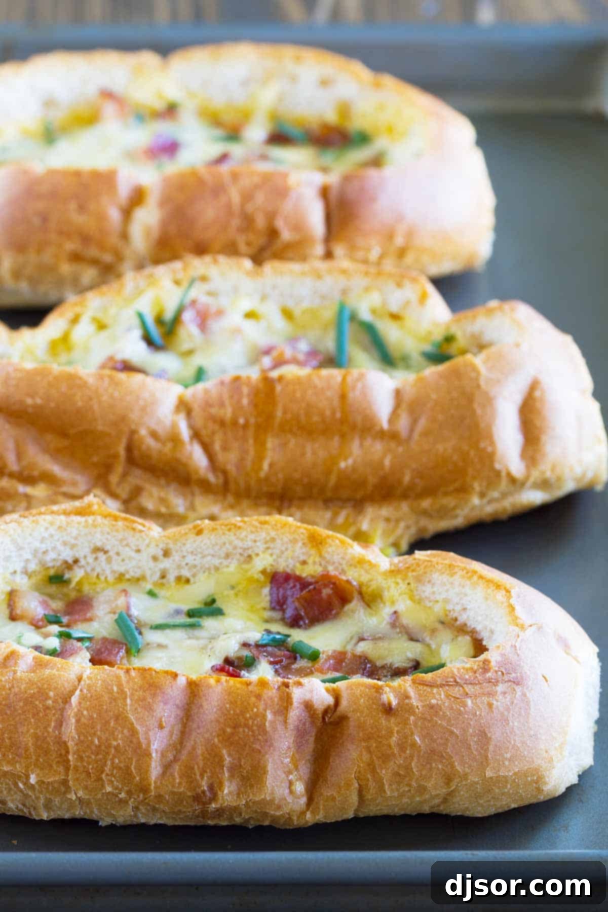 Ultimate Breakfast Bread Boats 4 Three golden-brown Baked Egg, Bacon, and Cheese Boats arranged on a baking sheet, freshly out of the oven and garnished with fresh chives, ready to be served.