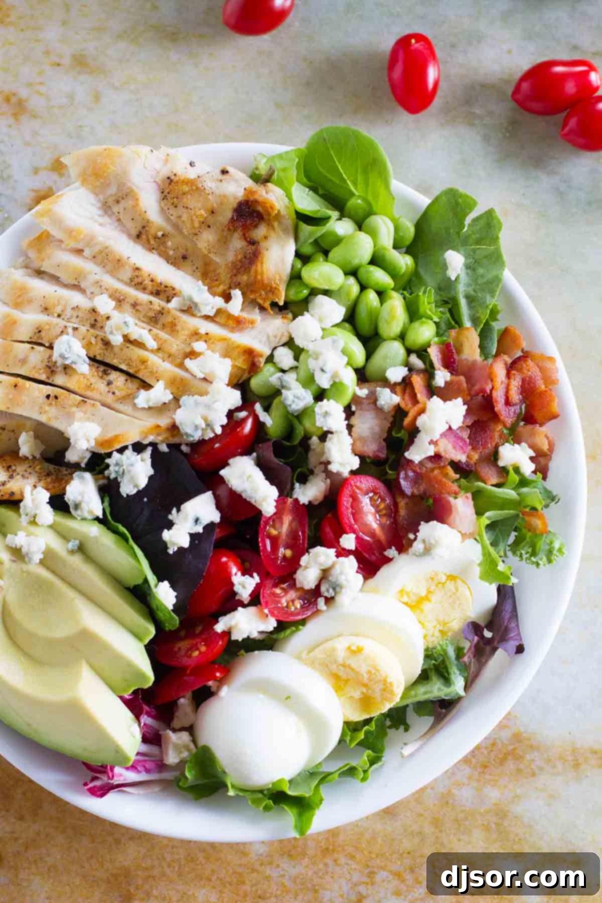 A vibrant Cobb salad featuring grilled chicken, ripe tomatoes, perfectly boiled eggs, green edamame, crispy bacon, and creamy avocado slices, all artfully arranged.