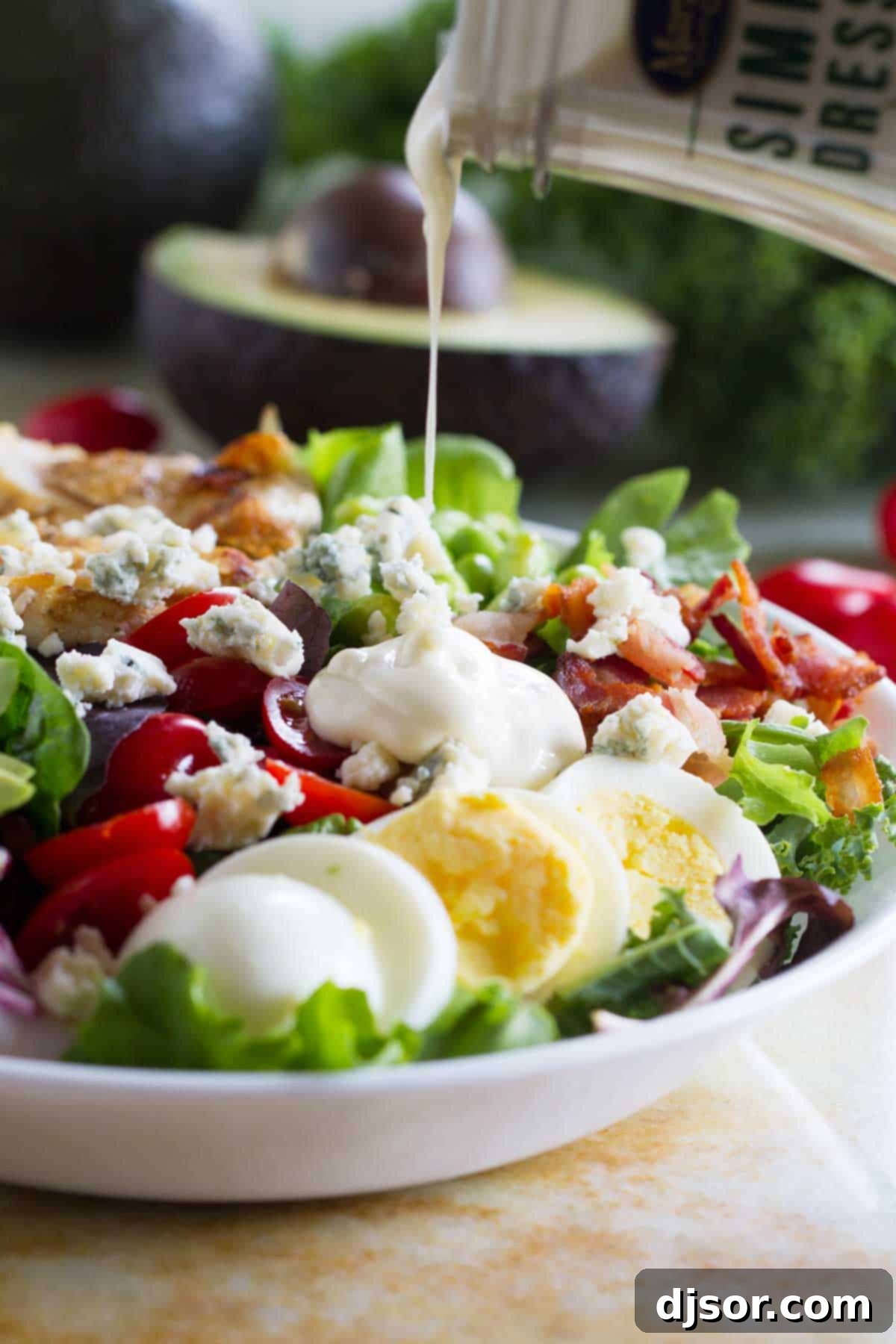 Close-up shot of ranch dressing being drizzled generously over a freshly prepared Protein-Packed Cobb Salad, highlighting its rich textures and vibrant colors.