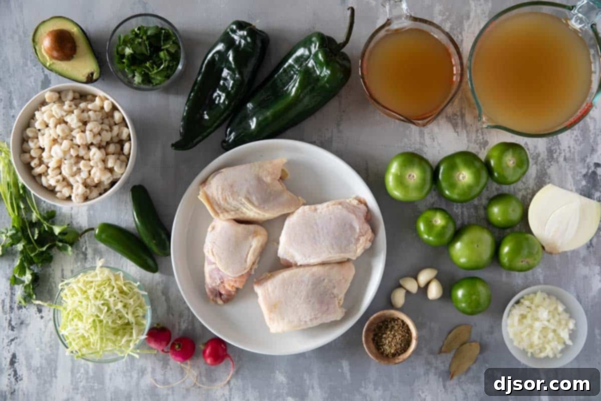 Zesty Green Pozole 3 Fresh ingredients laid out for Pozole Verde, including chicken thighs, poblano peppers, jalapeños, tomatillos, onion, garlic, cilantro, hominy, and a carton of chicken broth.