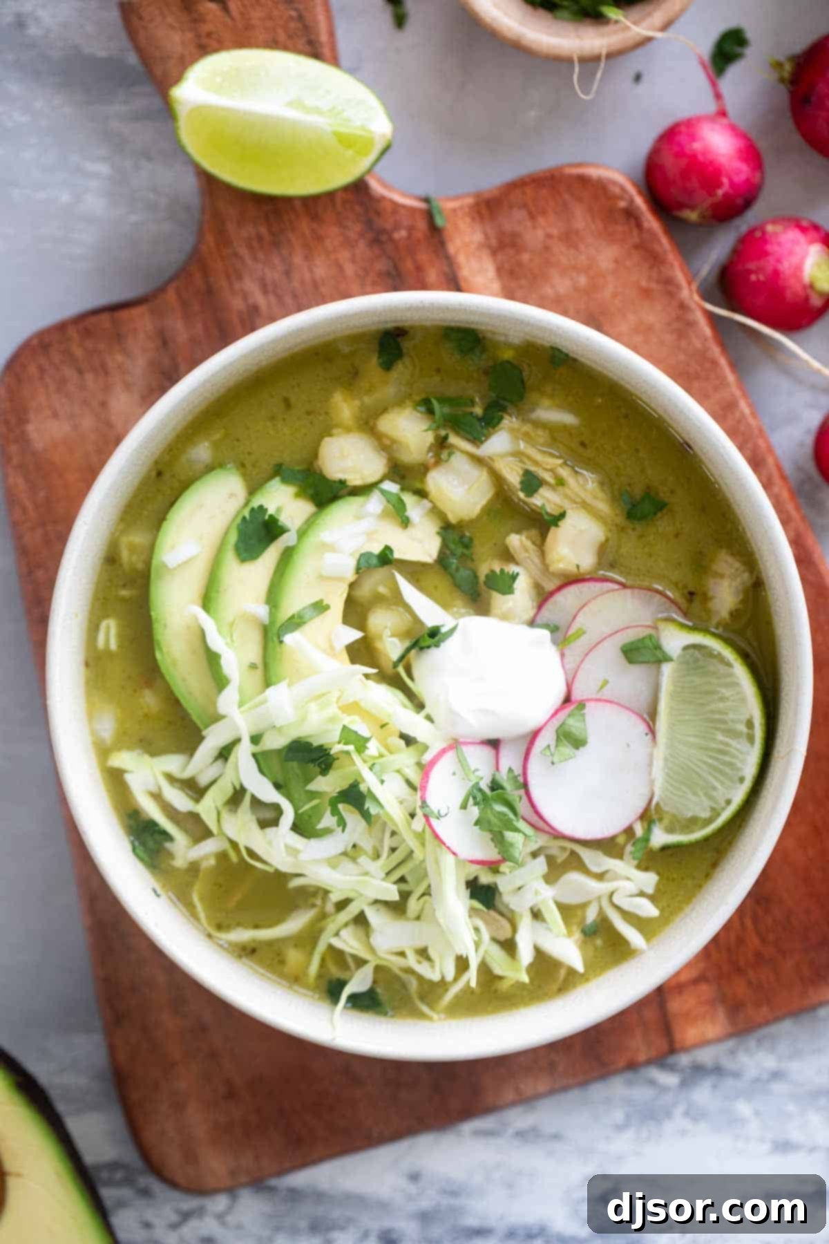 Zesty Green Pozole 9 A close-up of a rustic bowl of Pozole Verde, beautifully garnished with crisp shredded cabbage, bright red radishes, fresh green cilantro, and creamy slices of avocado, ready to be savored.