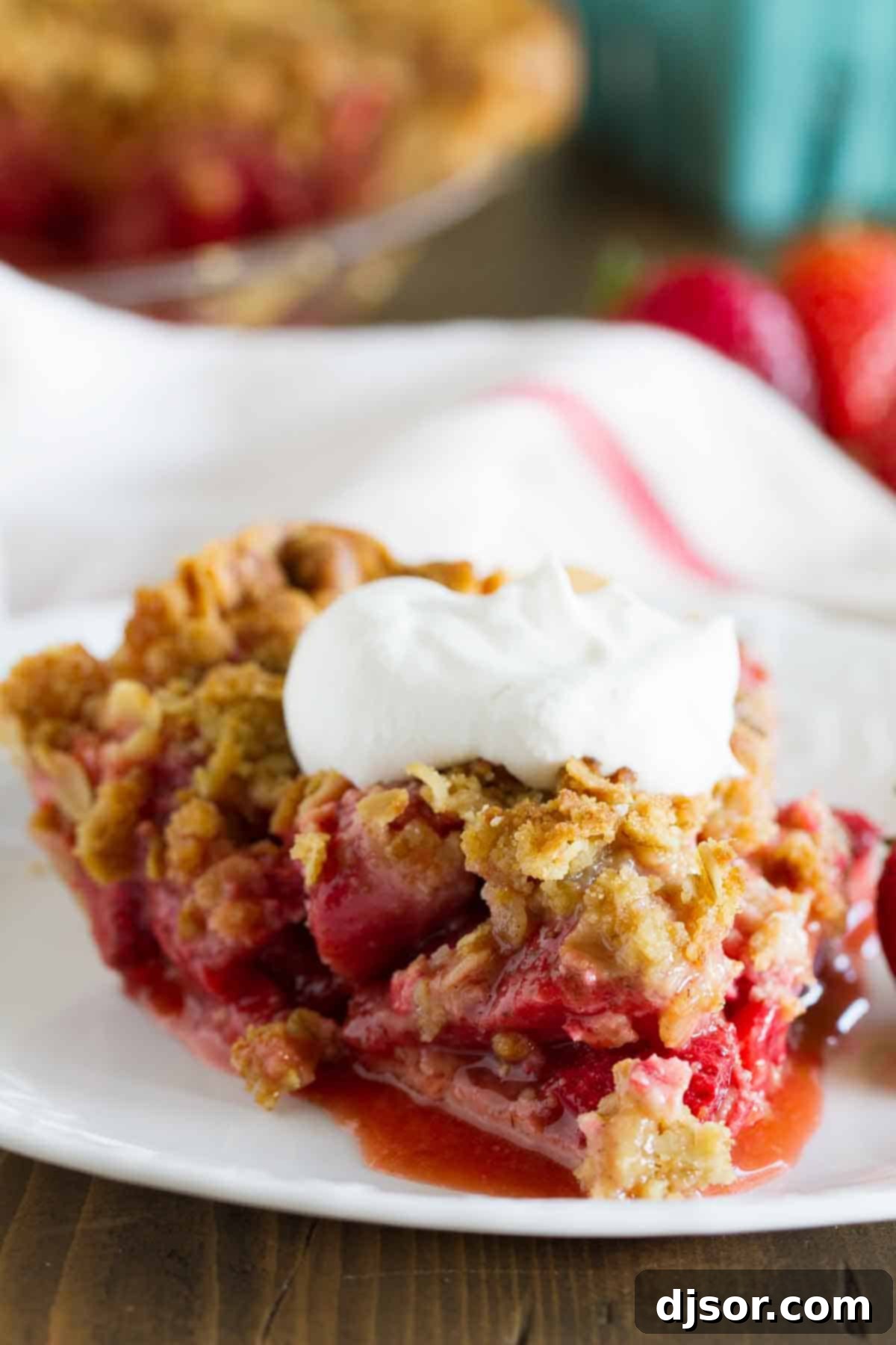 A delectable slice of Strawberry Crumble Pie, garnished with a generous dollop of freshly whipped cream.
