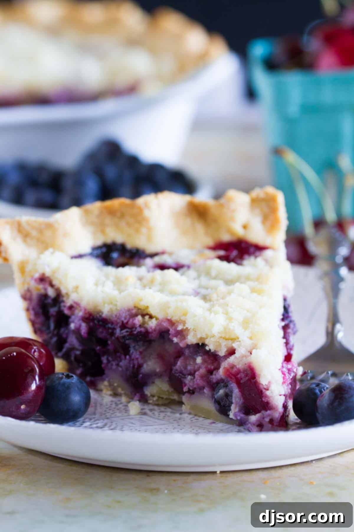 A beautiful slice of homemade Cherry and Blueberry Cream Pie on a white plate, showcasing the vibrant berries, creamy filling, and golden streusel topping.