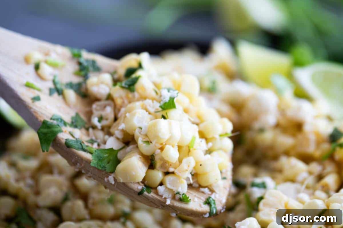 Take advantage of sweet summer corn with this Mexican Corn Salad - filled with Mexican cheese, lime, cilantro and a zing of spiciness. A wooden spoon scooping a portion of Mexican Corn Salad from a large bowl, highlighting its fresh ingredients.