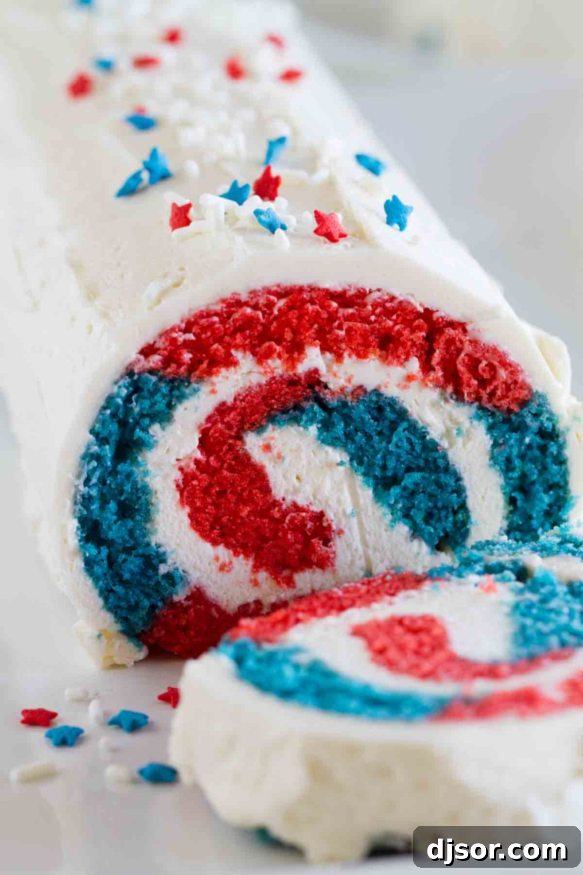 Red, white, and blue cake roll adorned with star sprinkles, sliced to reveal its patriotic interior