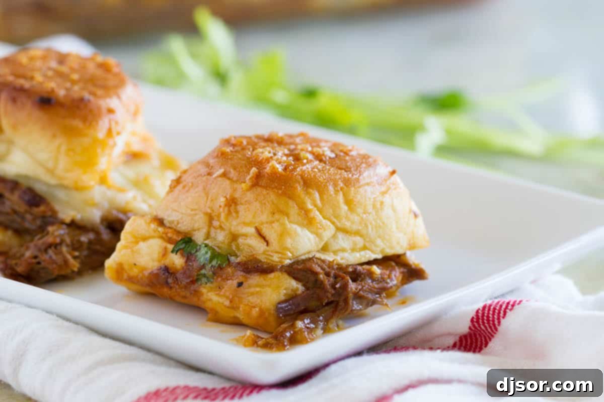 Individual Enchilada Beef Sliders on a plate, showcasing melted cheese and a flavorful topping.