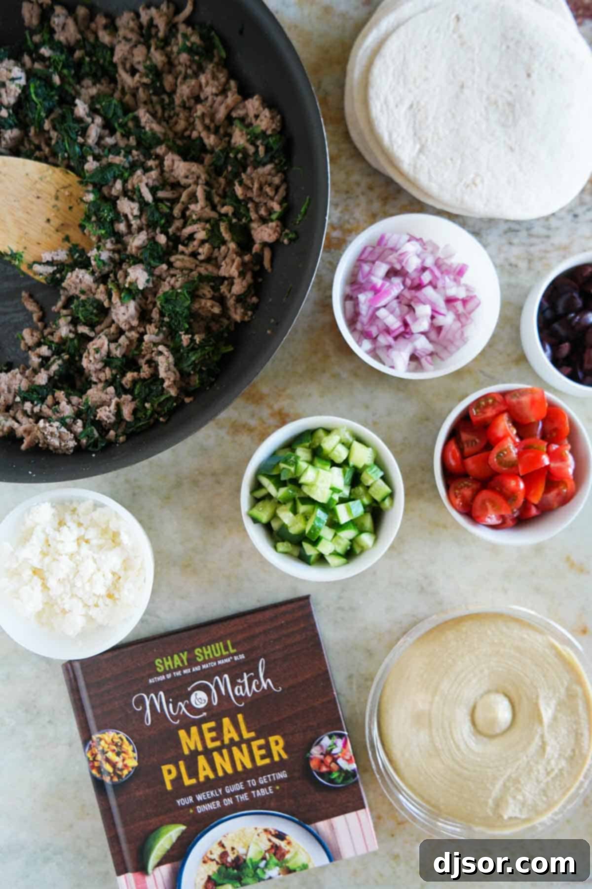 Souvlaki Shells 3 Fresh ingredients laid out on a wooden board, including ground turkey, fresh spinach, oregano, hummus, feta cheese, kalamata olives, red onion, cucumber, and cherry tomatoes, ready to make Greek Tacos.