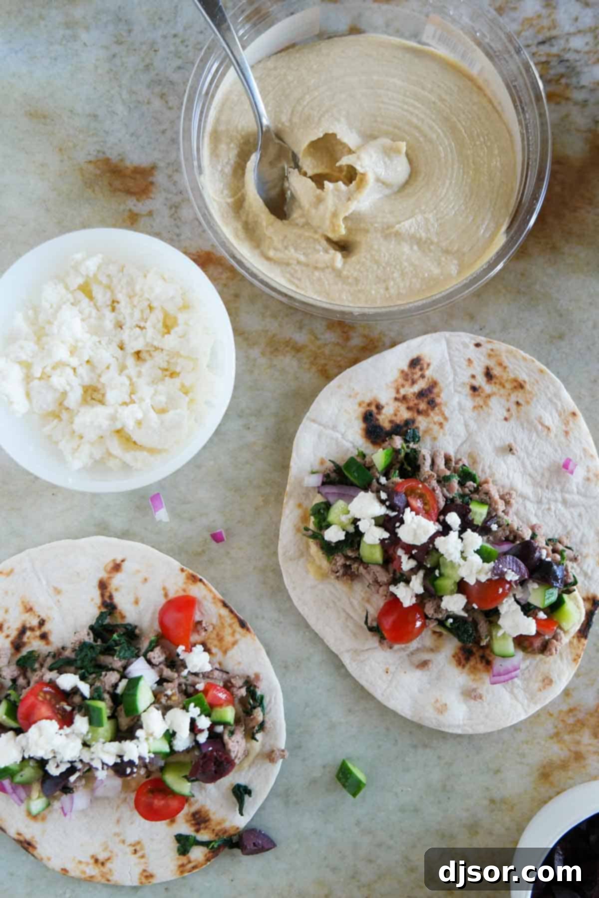 Souvlaki Shells 4 Close-up of a completed Greek taco on a flour tortilla, showcasing the vibrant layers of seasoned ground turkey, fresh spinach, creamy hummus, crisp vegetables, kalamata olives, and crumbled feta cheese.