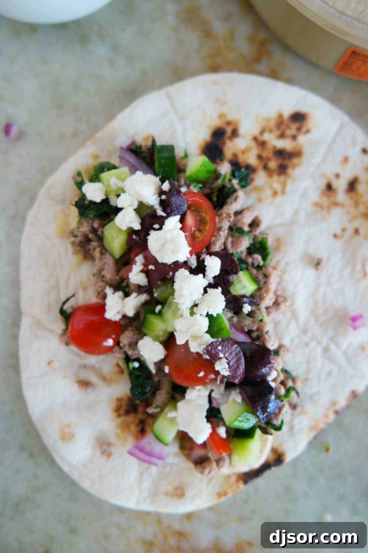 Souvlaki Shells 5 A single, perfectly assembled Greek taco on a flour tortilla, highlighting the rich filling and vibrant toppings, with a sprinkle of kalamata olives and feta cheese for a finishing touch.