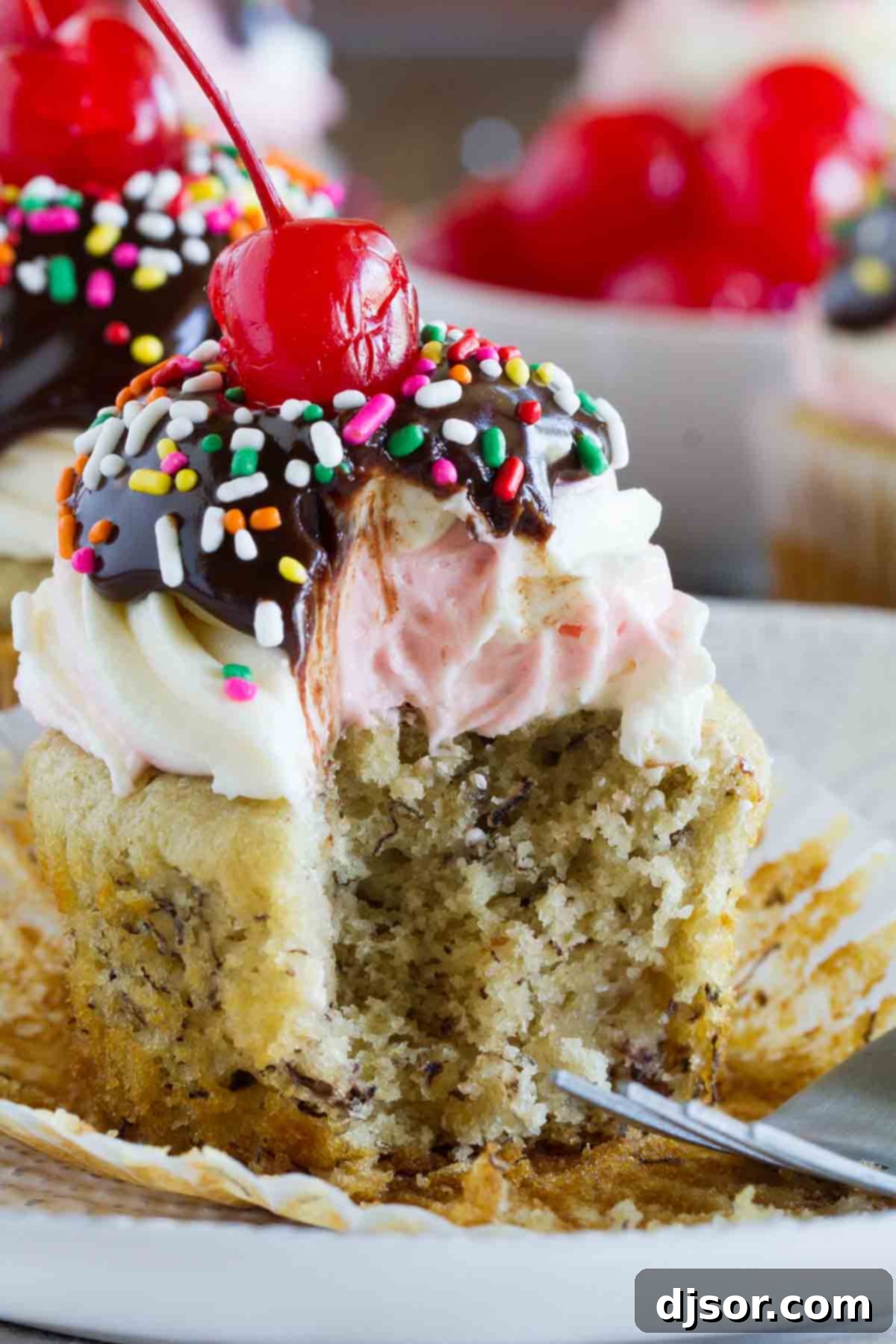 Close-up of a banana split cupcake with a small bite taken, revealing the moist cake texture and layered frosting