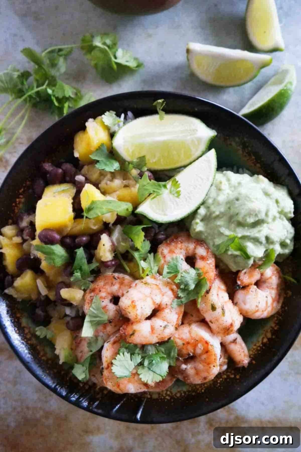 Beautifully assembled Spicy Shrimp Bowls, showcasing layers of coconut rice, seasoned shrimp, a colorful bean and fruit medley, and creamy avocado. Spicy Shrimp Bowls - coconut rice topped with shrimp, beans, mango, pineapple, and mashed avocado.