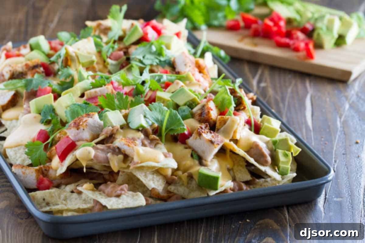 Whether for family dinner or game night, everyone will love these Grilled Chicken Nachos. Tortilla chips are topped with beans, taco seasoned grilled chicken, and an easy homemade cheese sauce in this easy, cheesy Tex-Mex recipe. baking tray with Grilled Chicken Nachos
