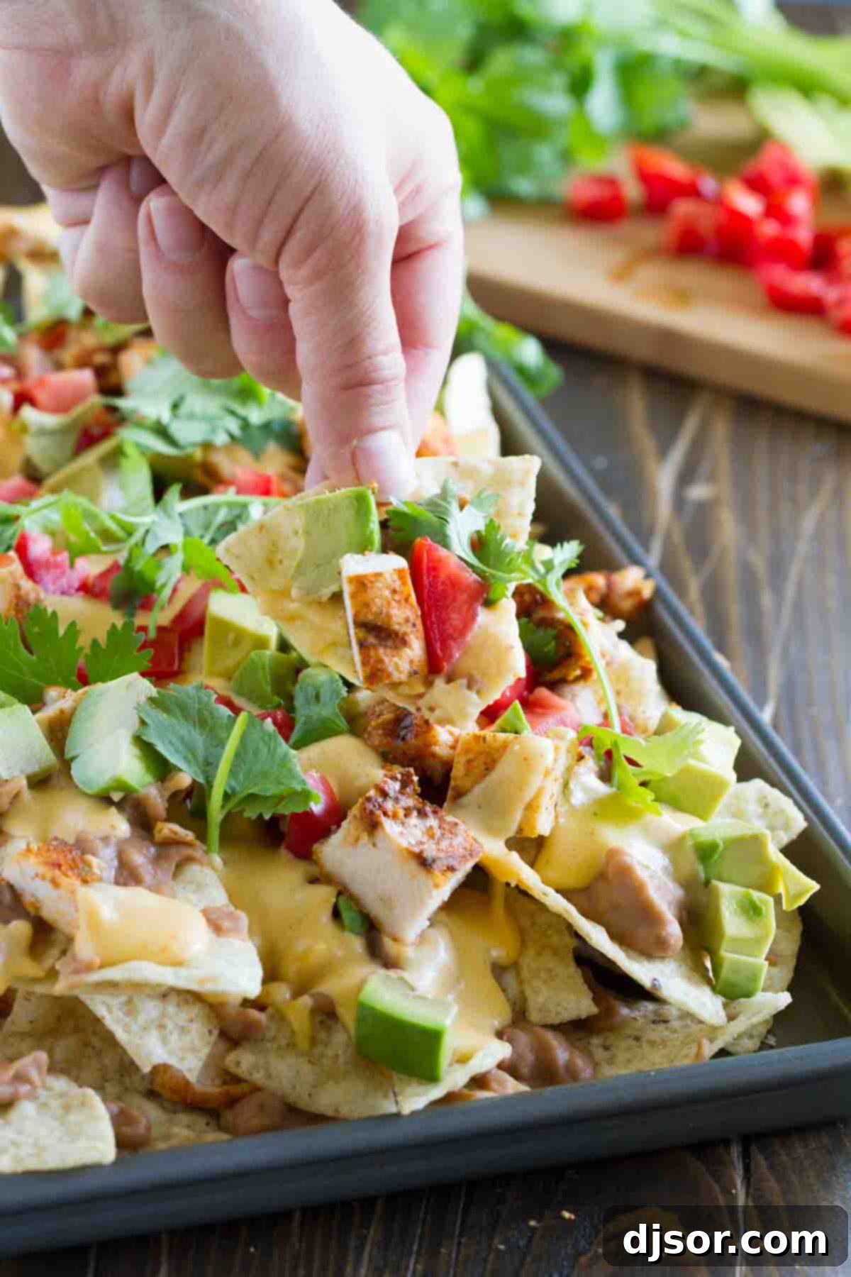 Whether for family dinner or game night, everyone will love these Grilled Chicken Nachos. Tortilla chips are topped with beans, taco seasoned grilled chicken, and an easy homemade cheese sauce in this easy, cheesy Tex-Mex recipe. hand with a chip filled with nacho toppings
