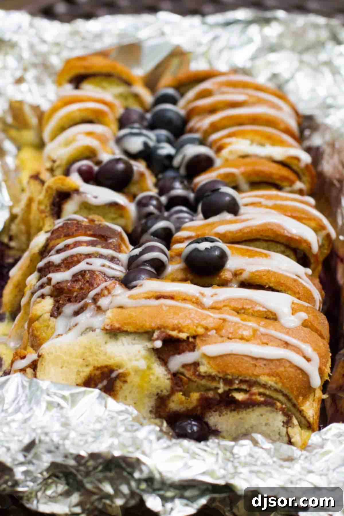loaf of campfire cinnamon blueberry bread in foil topped with blueberries and glaze