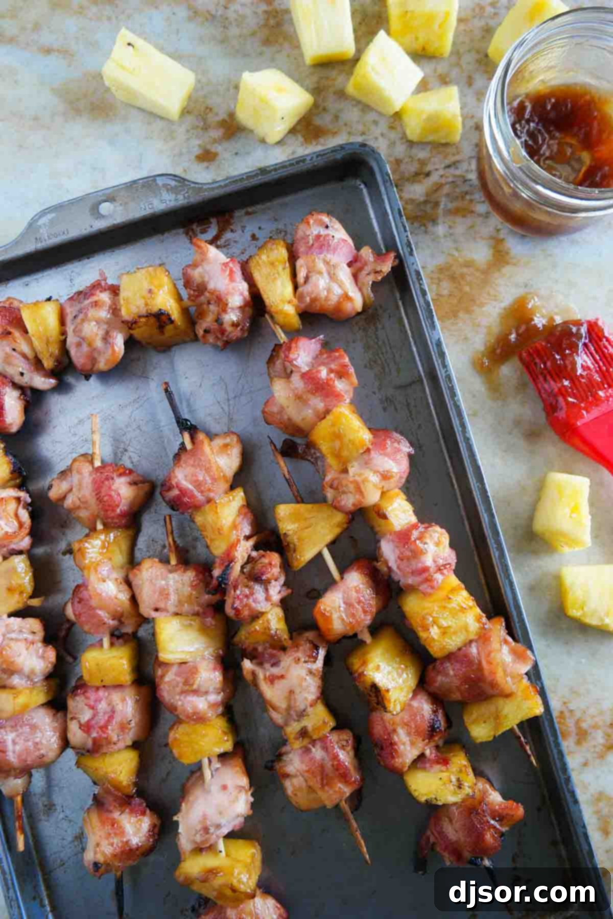 An appetizing overhead shot of uncooked Bacon Wrapped Teriyaki Chicken Skewers, beautifully arranged in a baking dish with pineapple chunks, ready for marination.