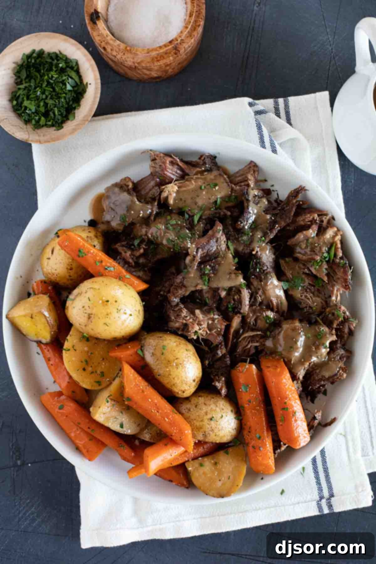 Sunday supper has never been so delicious! This Slow Cooker Pot Roast gives you perfectly tender beef, tasty (not mushy!) vegetables, and the most delicious gravy ever. Serving plate with chunks of pot roast with gravy and carrots and potatoes