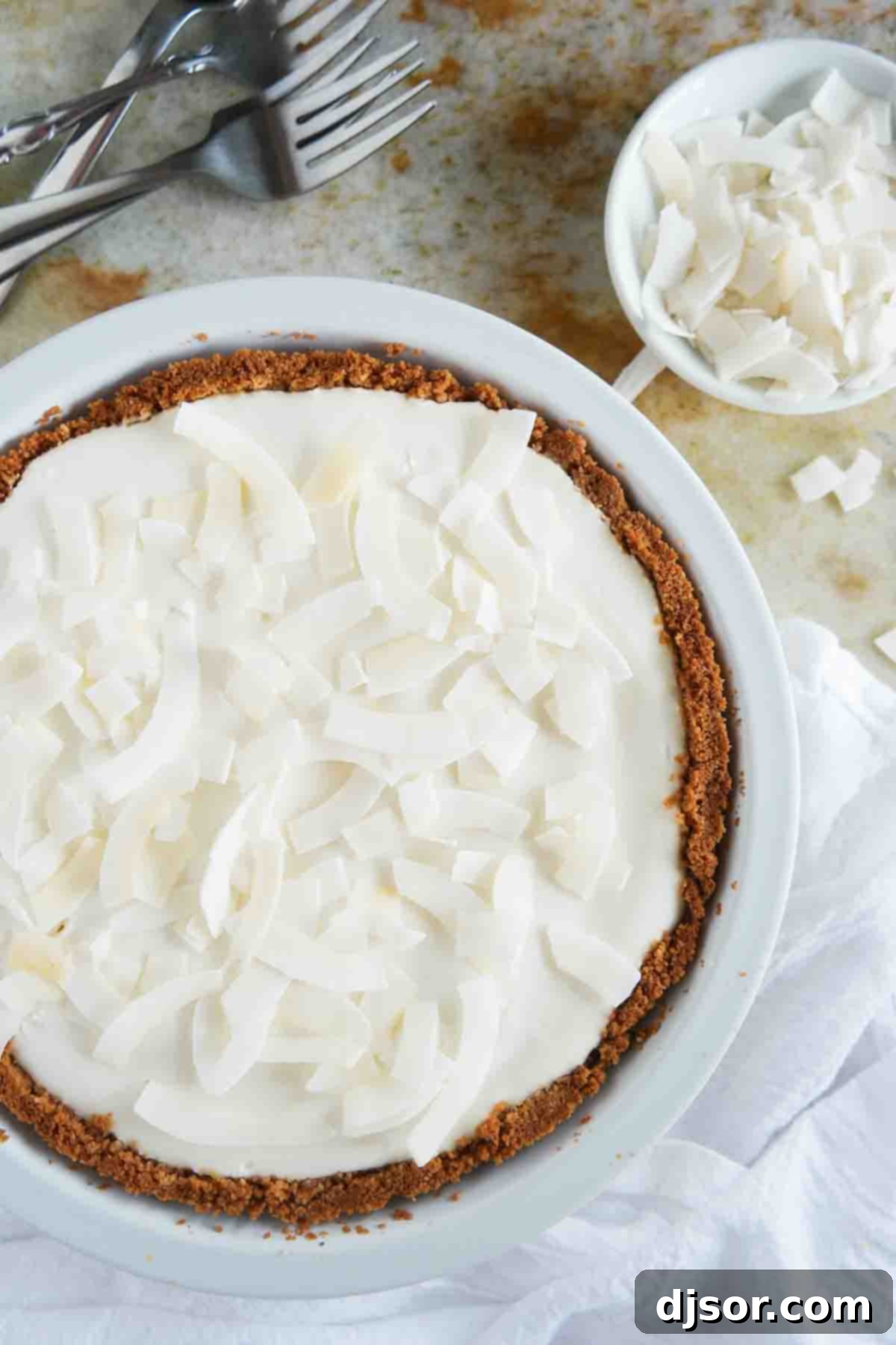 A close-up shot of the full Coconut Cheesecake Pie, featuring its perfectly golden graham cracker crust and the smooth, creamy texture of the filling prior to slicing.