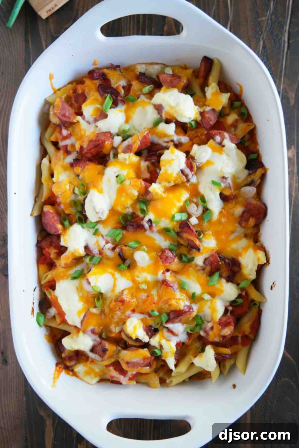 Layered Ingredients for Cheesy Kielbasa Pasta Casserole Close-up of pasta topped with kielbasa, a rich sauce, creamy ricotta cheese, and melted cheddar and mozzarella cheese, ready to be baked.