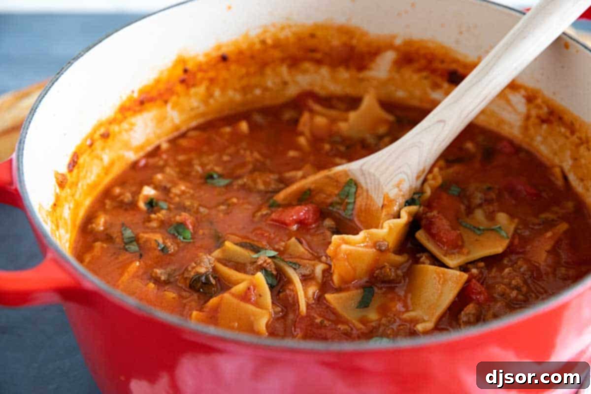 red dutch oven filled with lasagna soup with a wooden ladle
