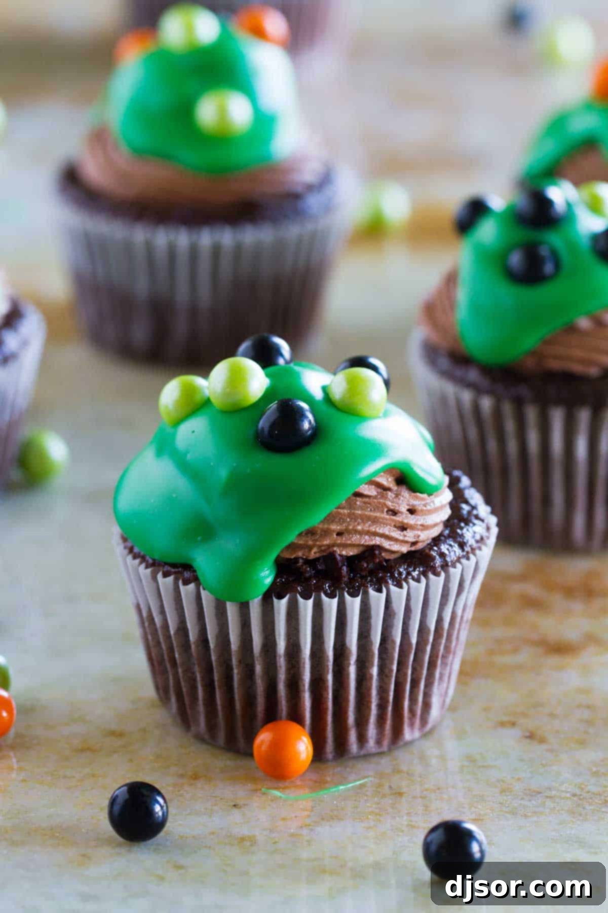 Close-up of Ultimate Chocolate Cupcakes, showcasing the decadent green ganache drip and festive candy ball toppings, ready for Halloween.