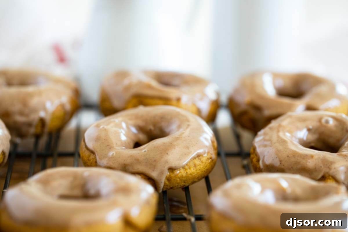 Baked Pumpkin Donuts with Maple Cinnamon Glaze arranged neatly on a cooling rack, showcasing their inviting texture and generous coating of glaze.