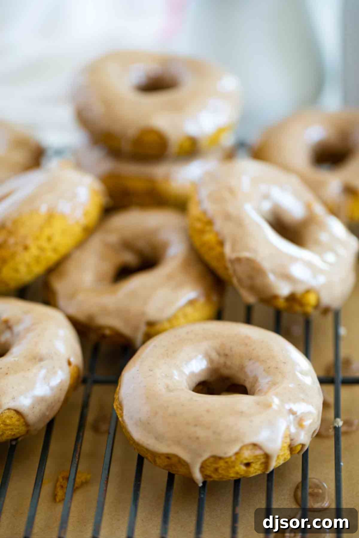 A stack of perfectly baked pumpkin donuts, glistening with maple cinnamon glaze, resting on a wire cooling rack.