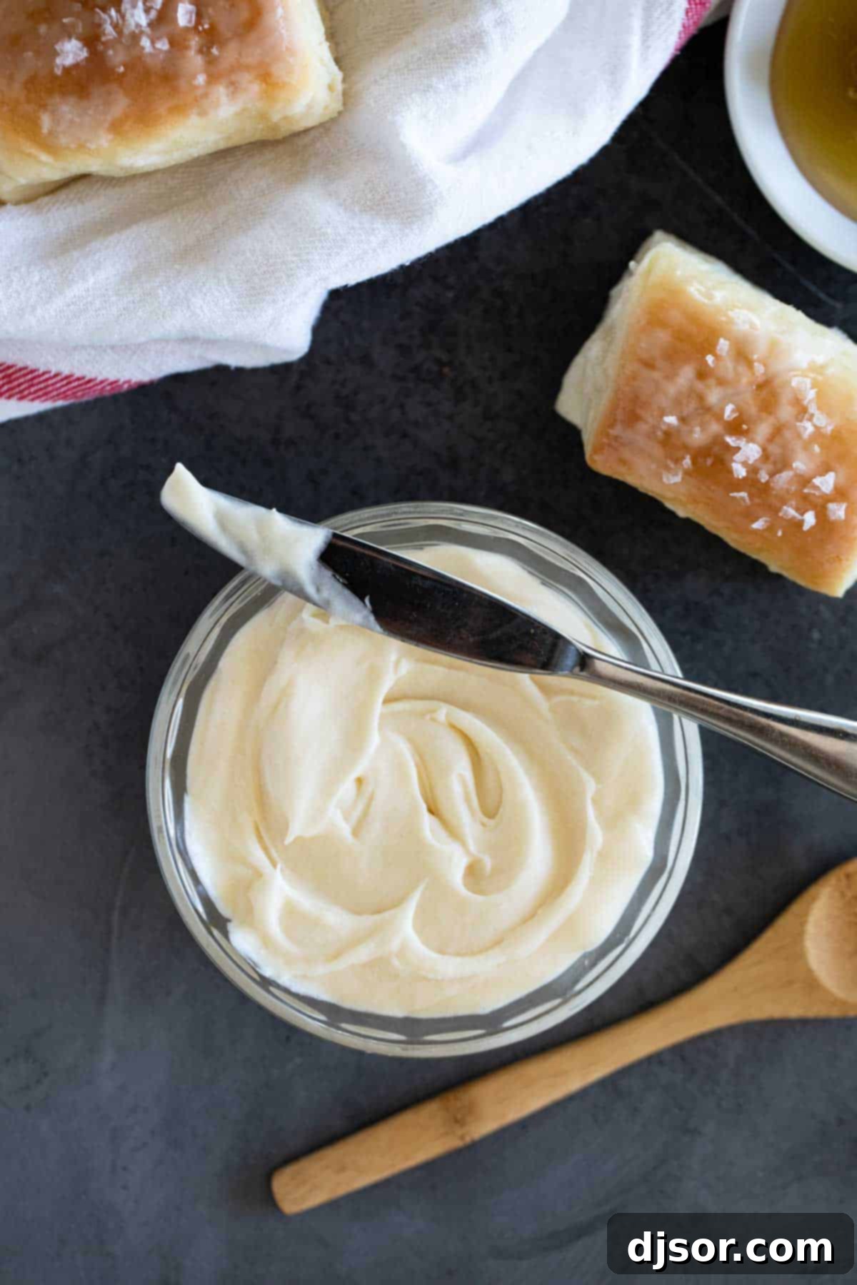 Perfect for slathering on homemade biscuits or rolls, this Honey Butter is going to be something that you always want in your refrigerator. Bowl of honey butter with fresh rolls beside it.