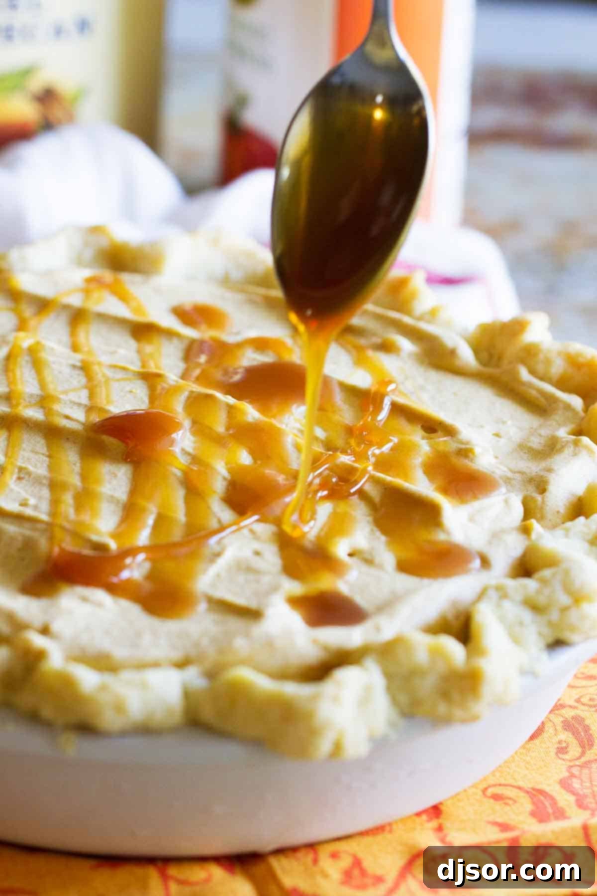 Creamy Autumn Delight Pumpkin Butter Pecan Ice Cream Pie 3 A close-up shot of caramel sauce being generously drizzled over the top of the frozen Pumpkin and Butter Pecan Ice Cream Pie, creating beautiful golden streams against the creamy surface. This step adds both visual appeal and an irresistible sweetness to the dessert.