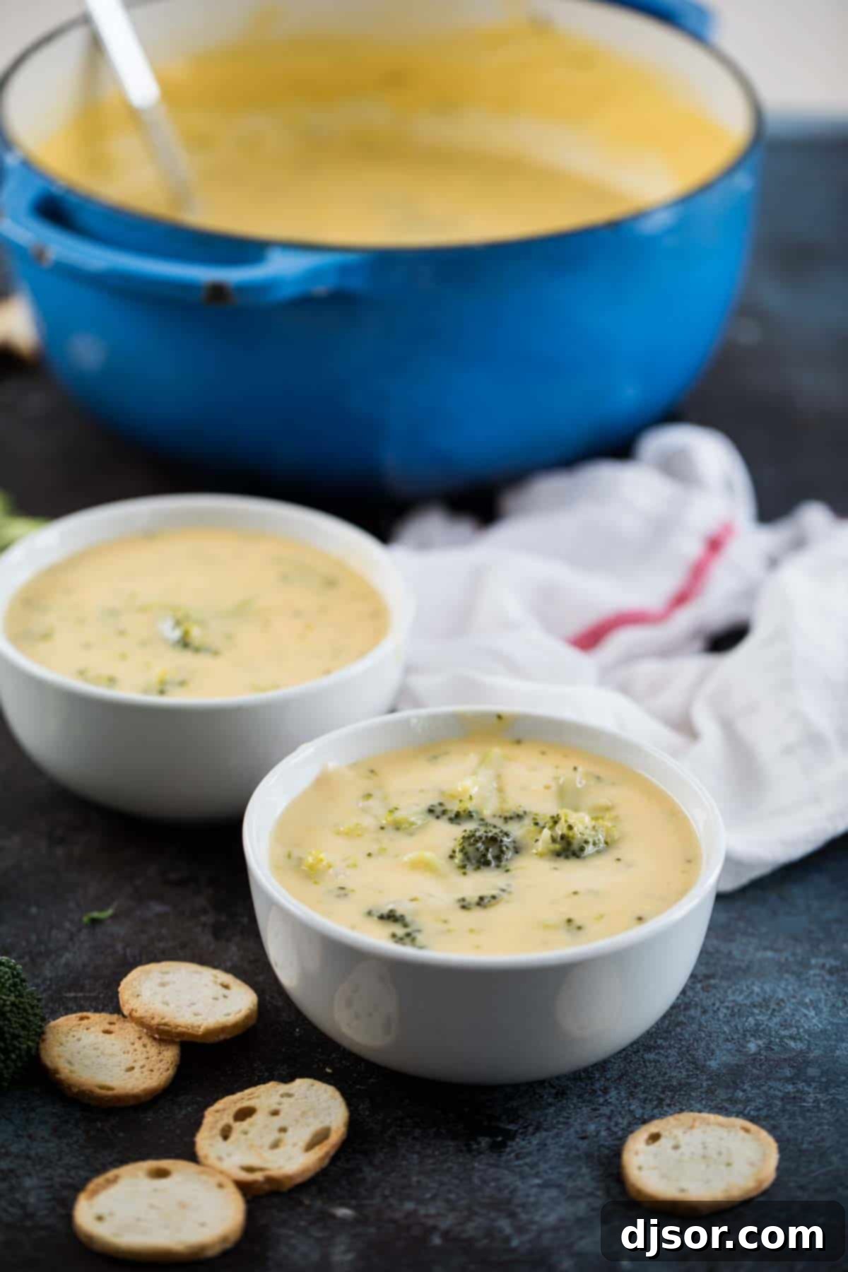 Two bowls of creamy broccoli cheese soup with a pot in the background, ready to be served on a cozy evening.