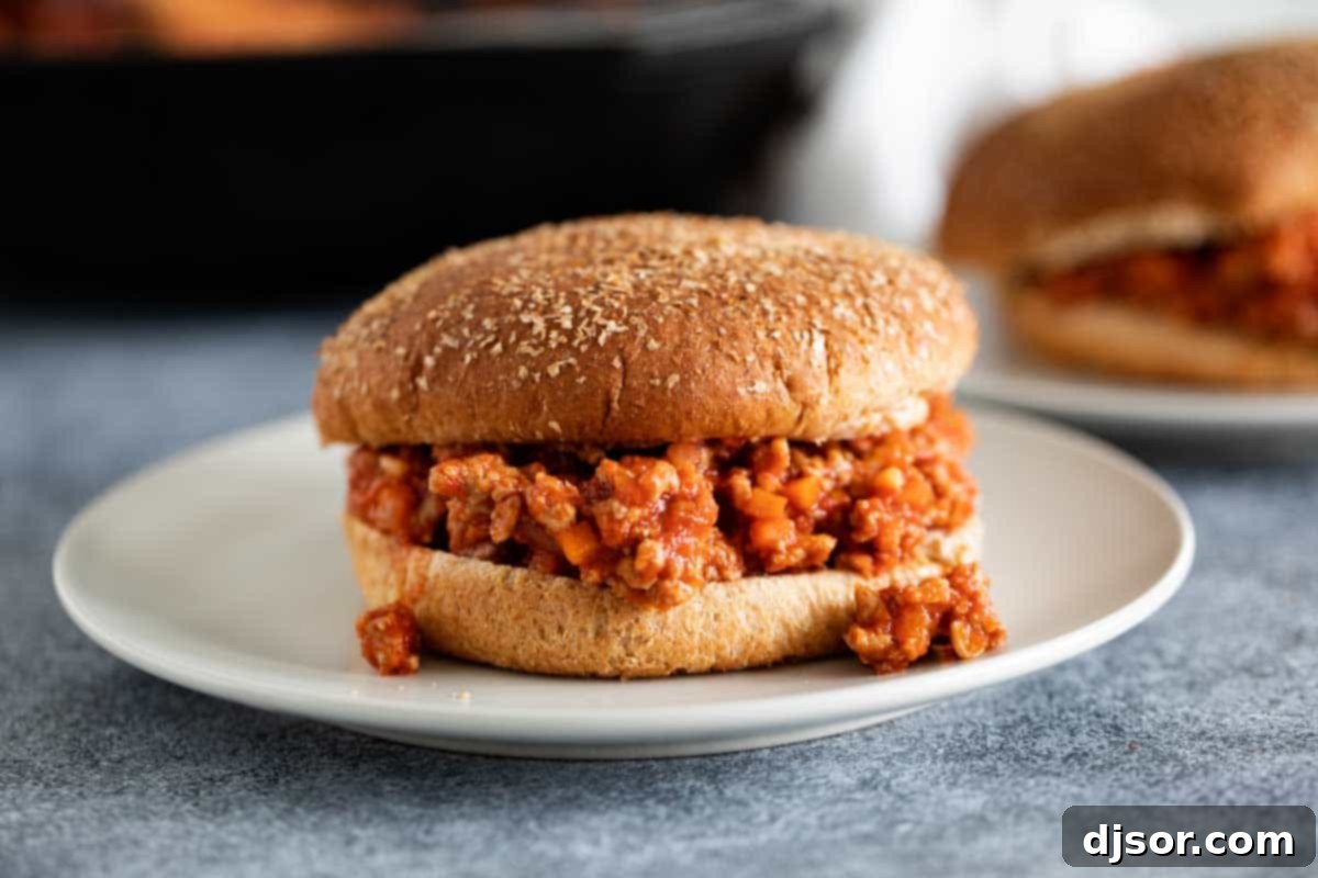 Healthy Turkey Sloppy Joes: A Flavorful and Easy Ground Turkey Recipe A single turkey sloppy joe served on a whole wheat bun, resting on a rustic white plate with a side of fresh greens, showcasing its rich, savory filling.