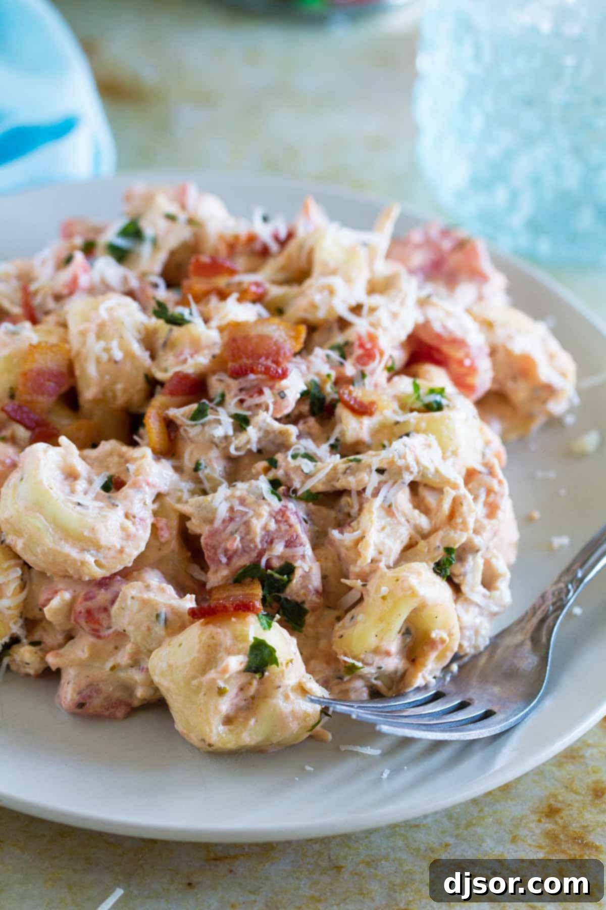 A vibrant serving of Creamy Tomato Tortellini with Chicken and Bacon, garnished with fresh herbs and a fork, ready to be enjoyed as a delightful weeknight meal.