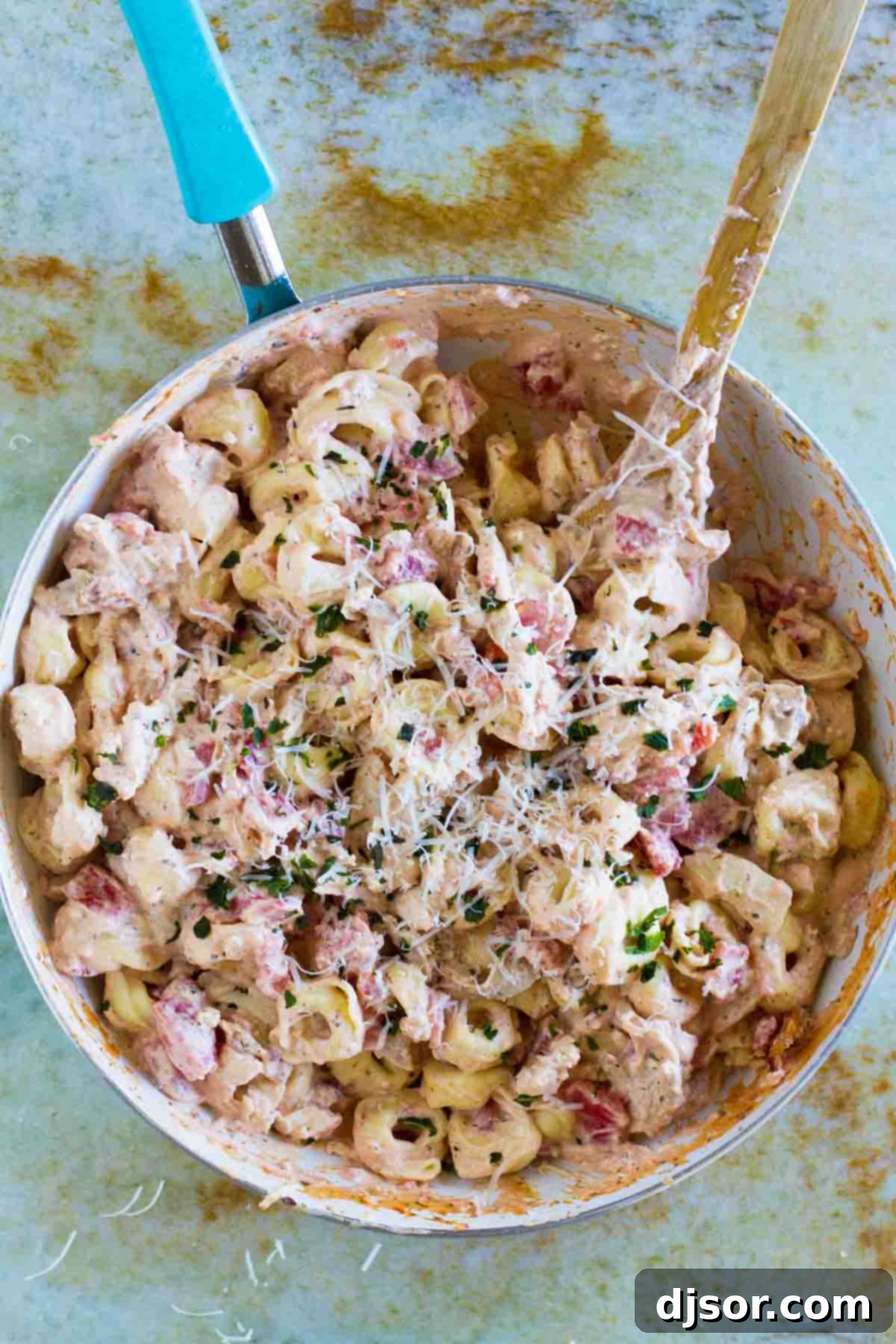 A large skillet brimming with Creamy Tomato Tortellini with Chicken and Bacon, topped generously with freshly grated parmesan cheese and ready to serve, highlighting the rich and inviting texture of the dish.