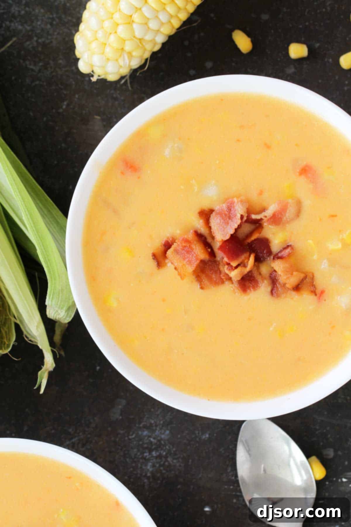 Hearty Corn and Bacon Chowder 4 Serving of Corn Chowder with Bacon in a white bowl, garnished with a sprinkle of crispy bacon and chives. Perfect for using fresh or frozen corn.