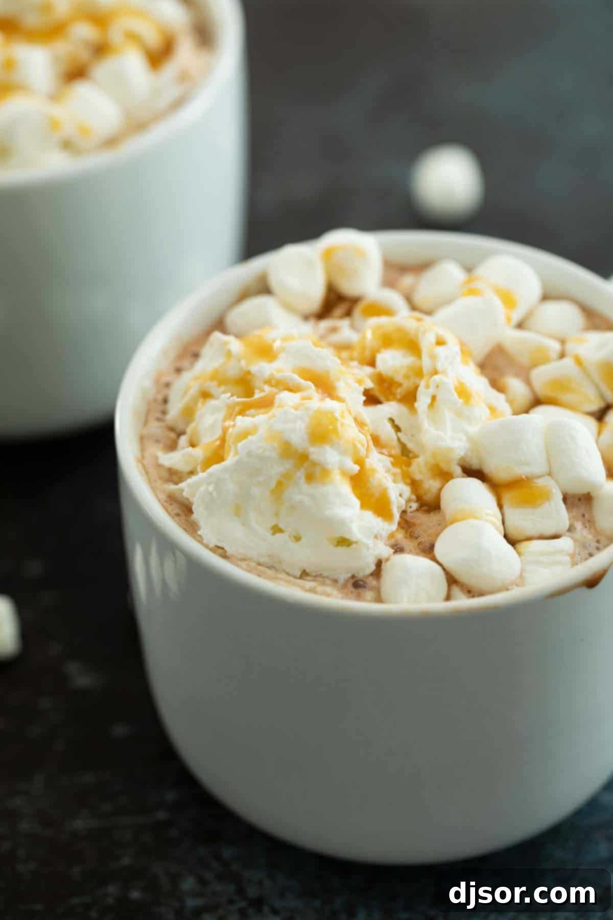 A close-up of a Salted Caramel Hot Chocolate mug, generously topped with swirling whipped cream and a delicate drizzle of caramel sauce, highlighting its luxurious texture and appeal.