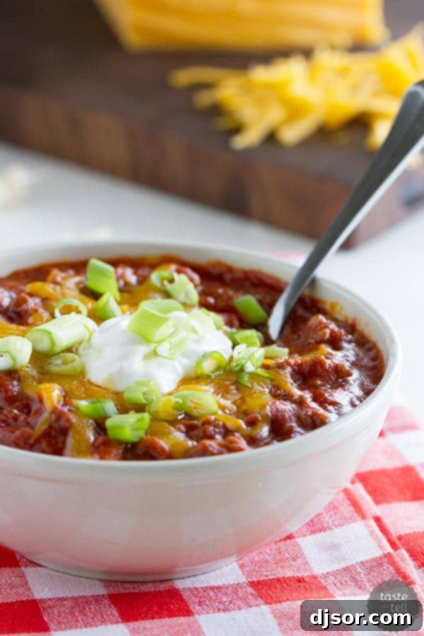 A steaming bowl of Flatlander Chili, rich with beef, sausage, and beans, topped with a dollop of sour cream and fresh cilantro.