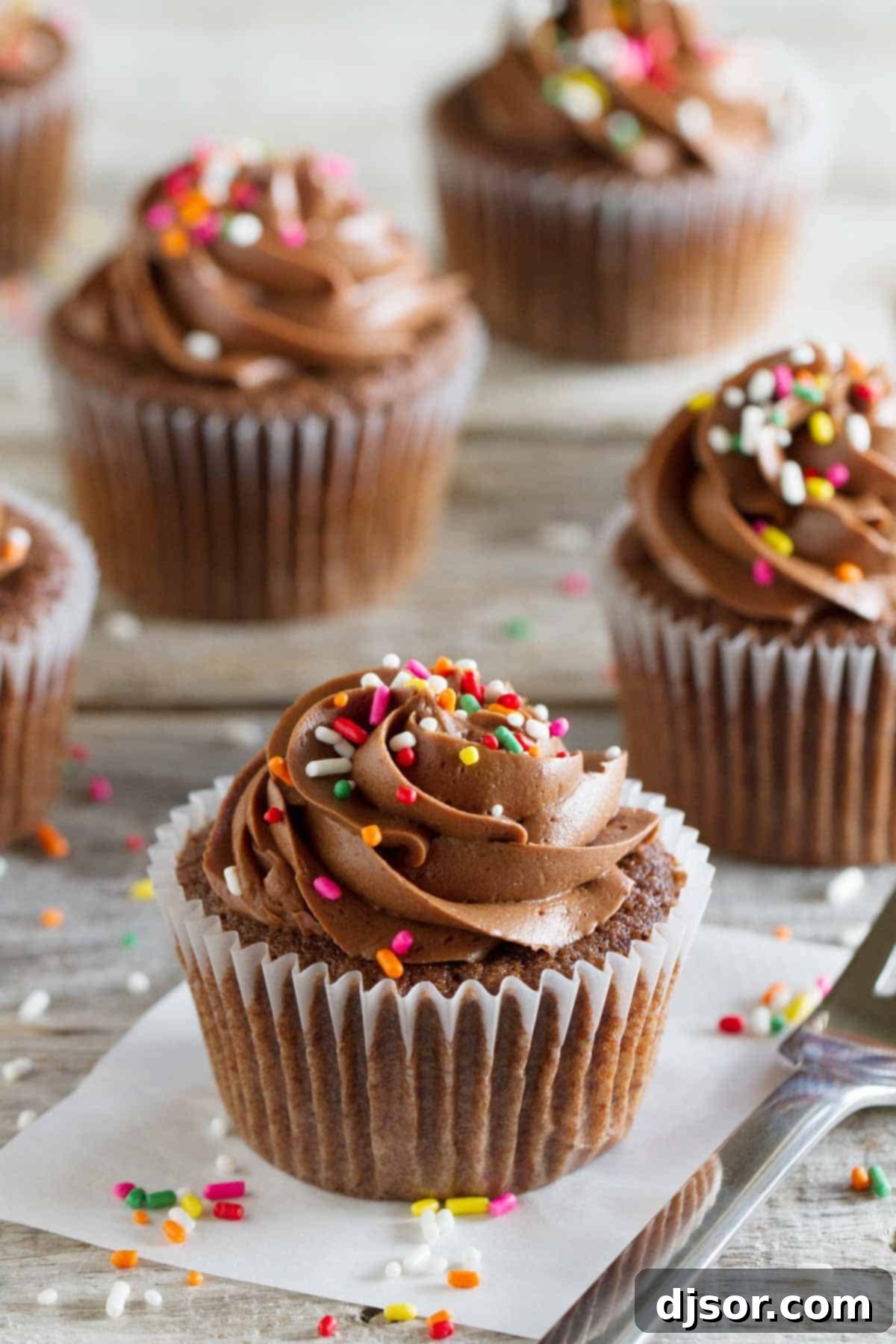 Decadent Chocolate Sour Cream Cupcakes with generous swirls of chocolate buttercream and colorful rainbow sprinkles, presented on a rustic wooden surface.