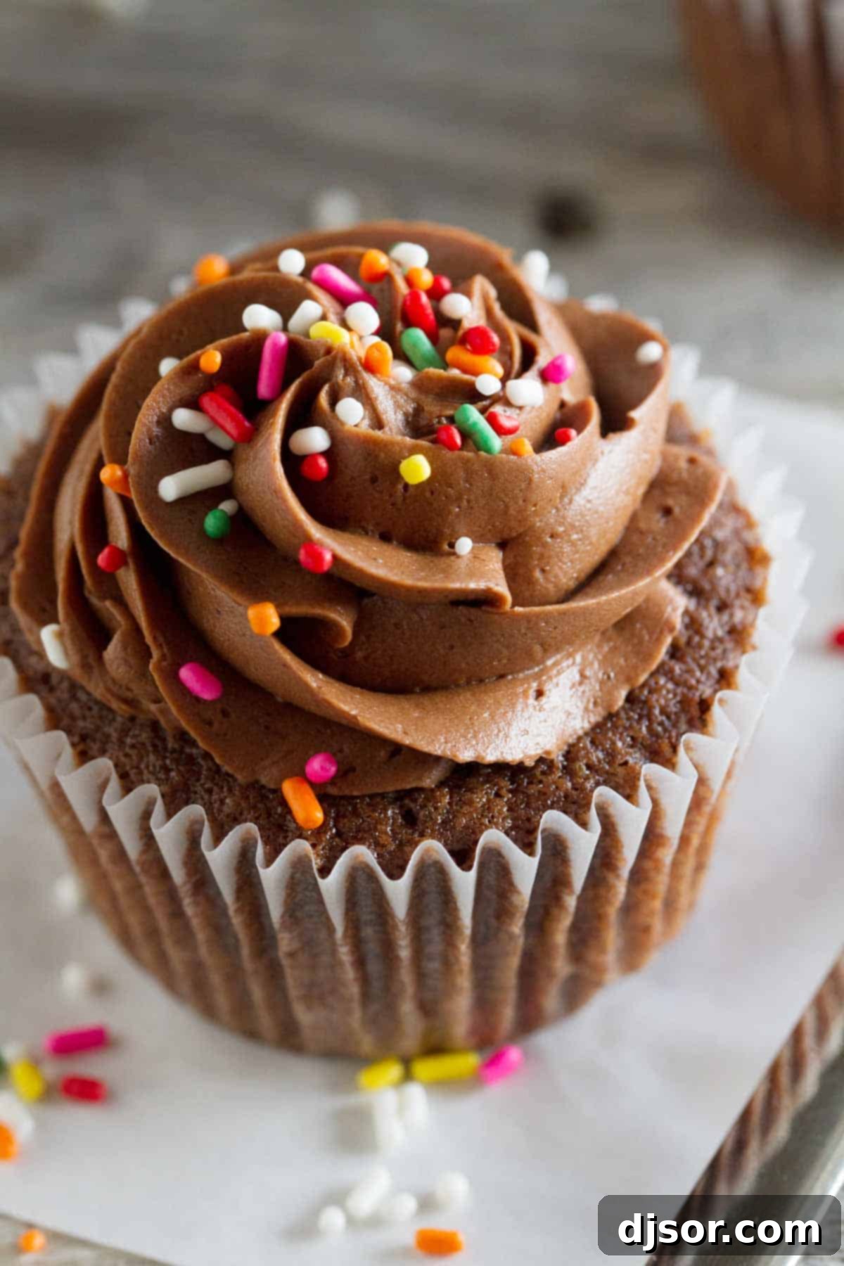 Close-up of a single Chocolate Sour Cream Cupcake, beautifully topped with creamy chocolate buttercream and vibrant rainbow sprinkles, ready to be enjoyed.