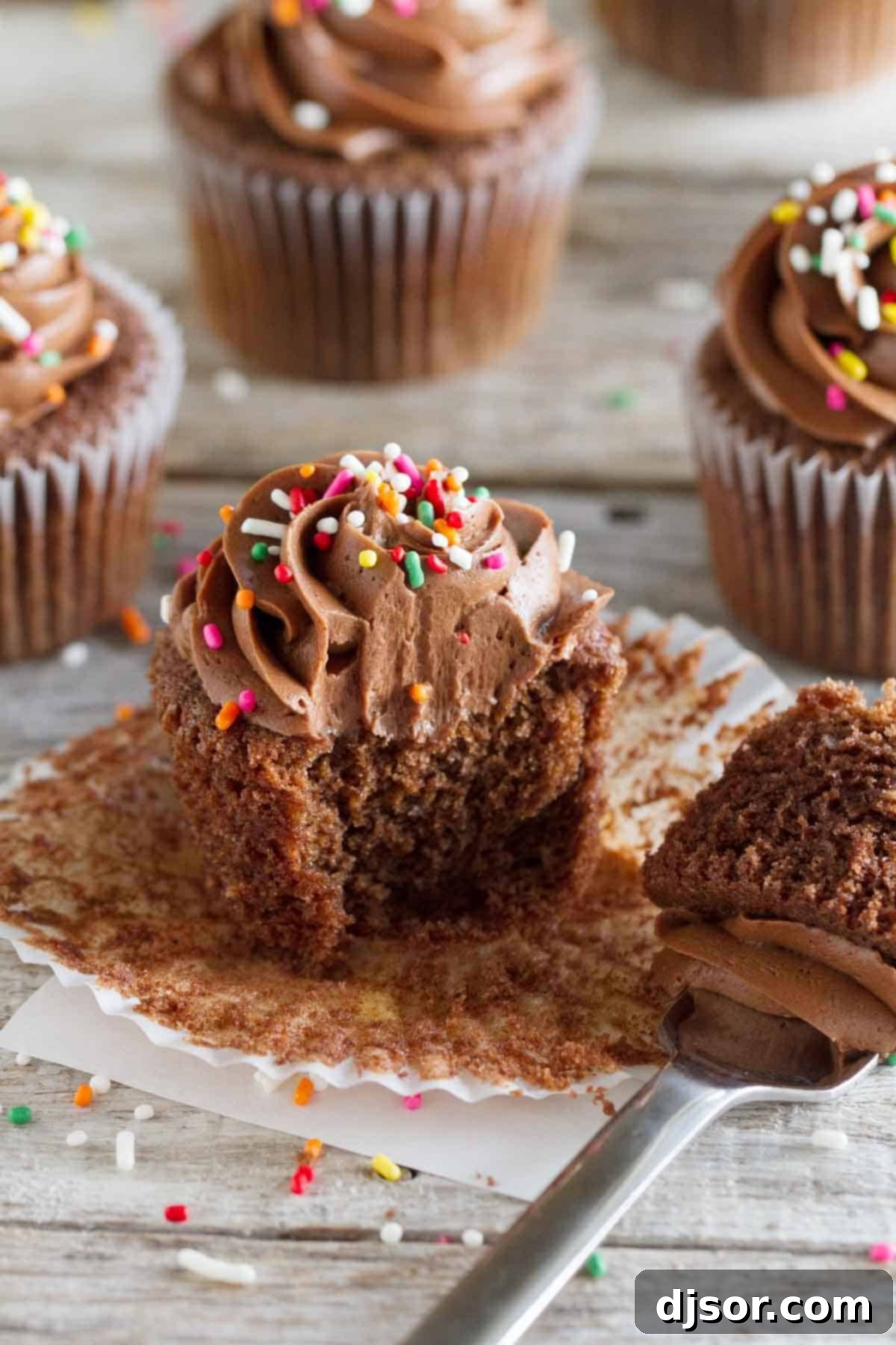 A delicious Chocolate Sour Cream Cupcake with a bite taken, showcasing its moist interior and rich chocolate buttercream, alongside other frosted cupcakes.