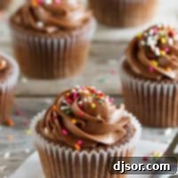 Chocolate Sour Cream Cupcakes with Chocolate Buttercream and rainbow sprinkles on a wooden surface.