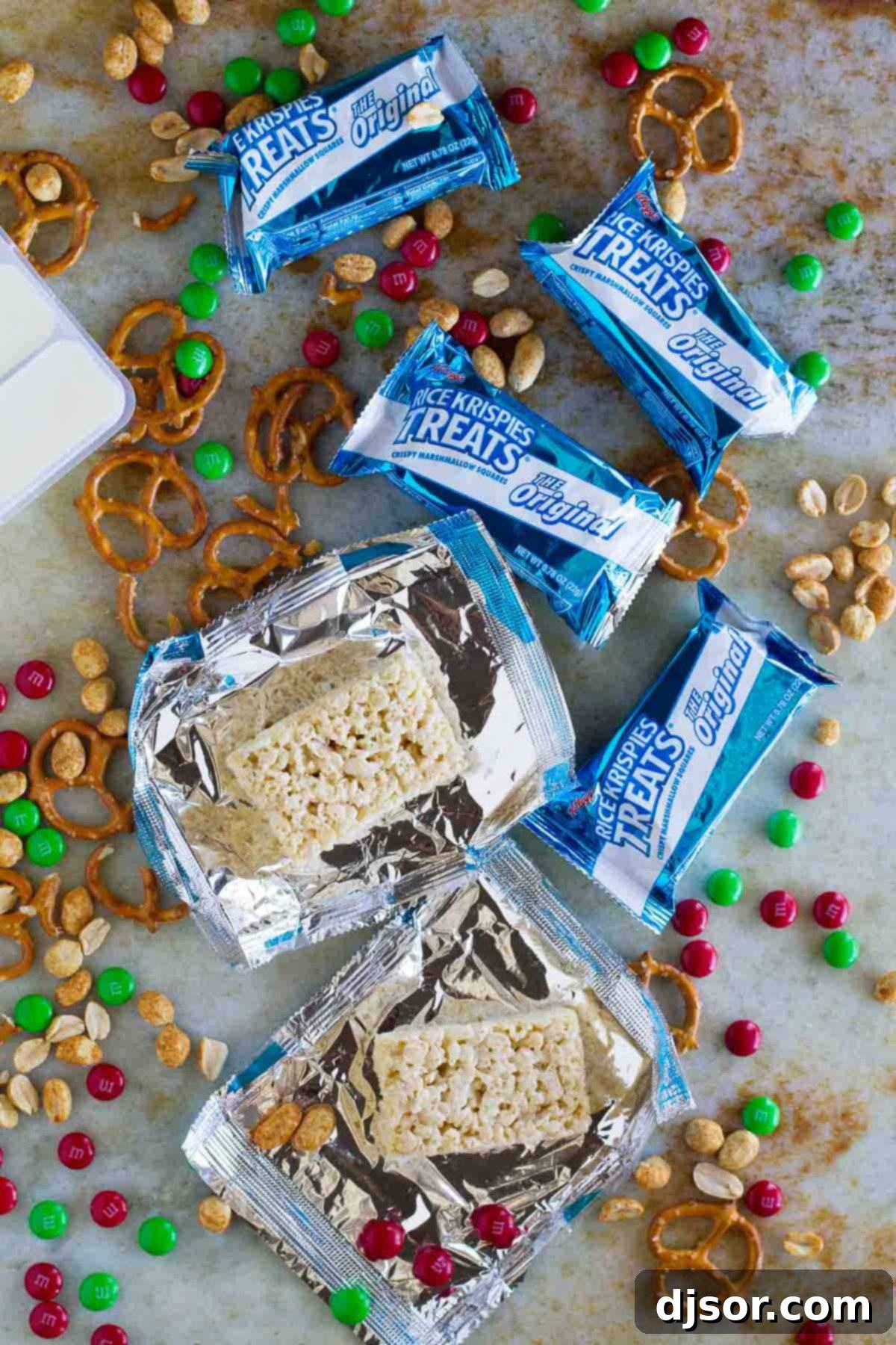 A flat lay of all the simple ingredients for the Sweet and Salty Christmas Mix: Rice Krispies treats, pretzels, holiday M&M's, peanuts, and vanilla candy coating.