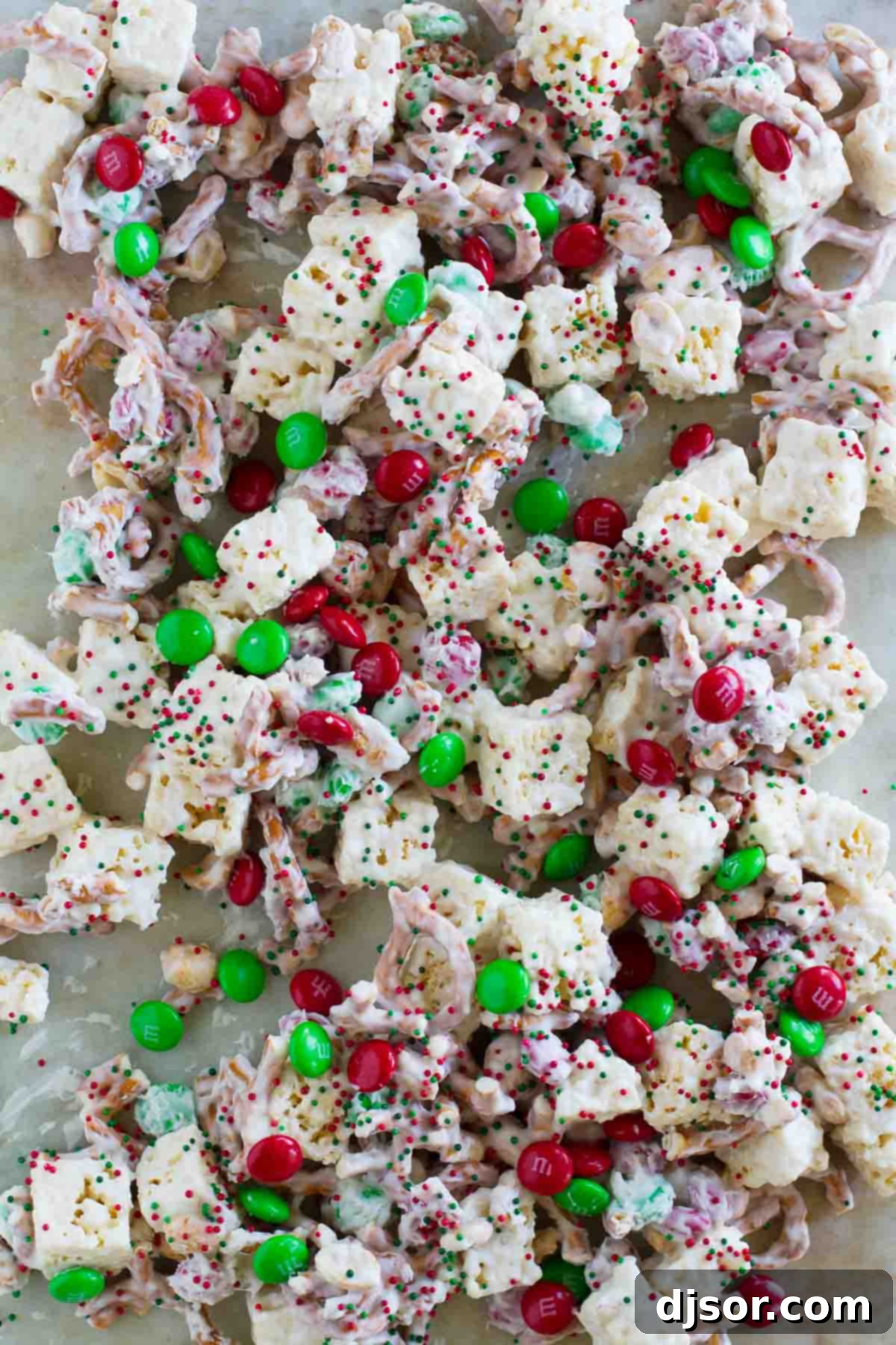 Sweet and Salty Christmas Mix spread out on waxed paper, adorned with holiday sprinkles and extra candies, cooling down.