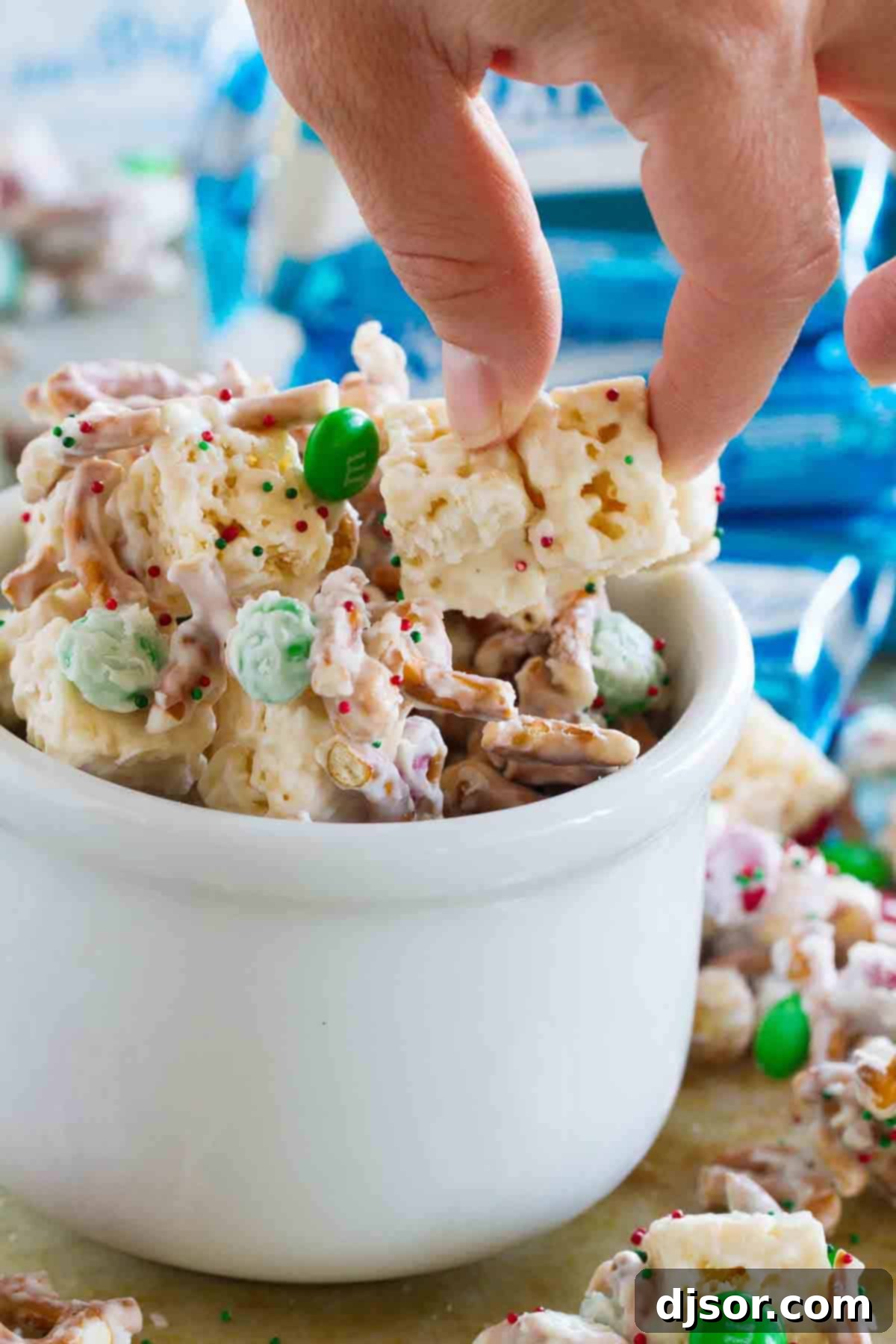 A hand reaches into a bowl of Sweet and Salty Christmas Mix, showcasing the various components and their festive appeal.
