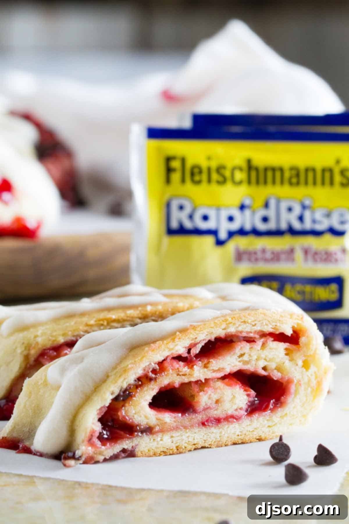 A baked Chocolate Cherry Roll, glistening with a delicate white glaze drizzled over its golden-brown surface, resting on a cooling rack.