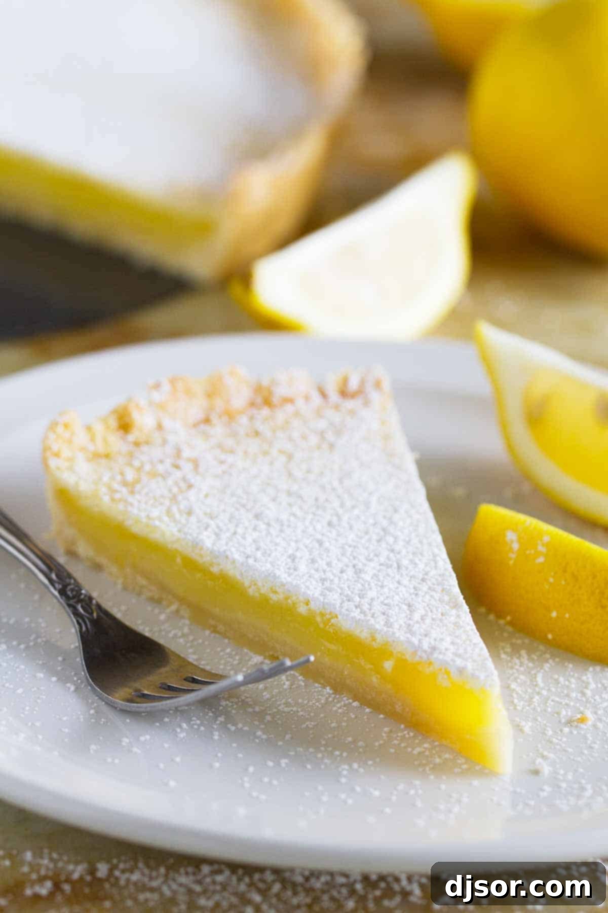 A perfectly sliced Shortbread Lemon Tart on a pristine white plate, showcasing its vibrant yellow filling and golden shortbread crust, ready to be enjoyed.