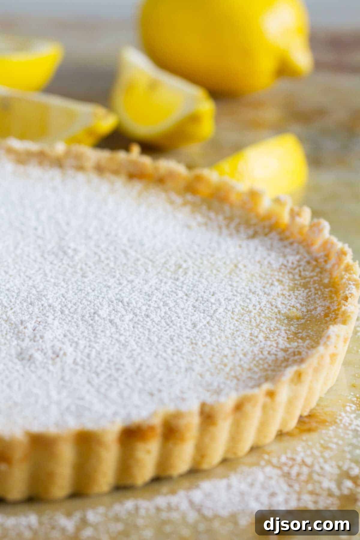 A full Shortbread Lemon Tart, delicately dusted with powdered sugar, sitting on a wooden surface, inviting you to cut into its sweet and tangy layers.
