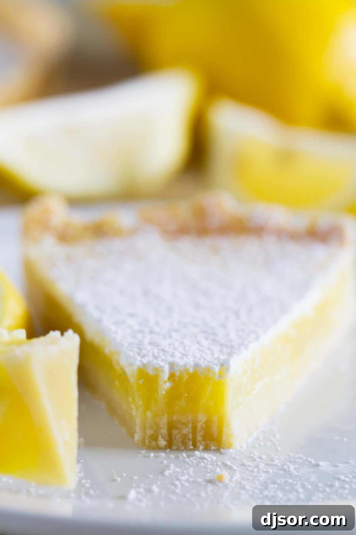 A close-up shot of a Shortbread Lemon Tart slice with a bite taken, revealing its smooth, bright yellow filling and the crumbly shortbread crust.