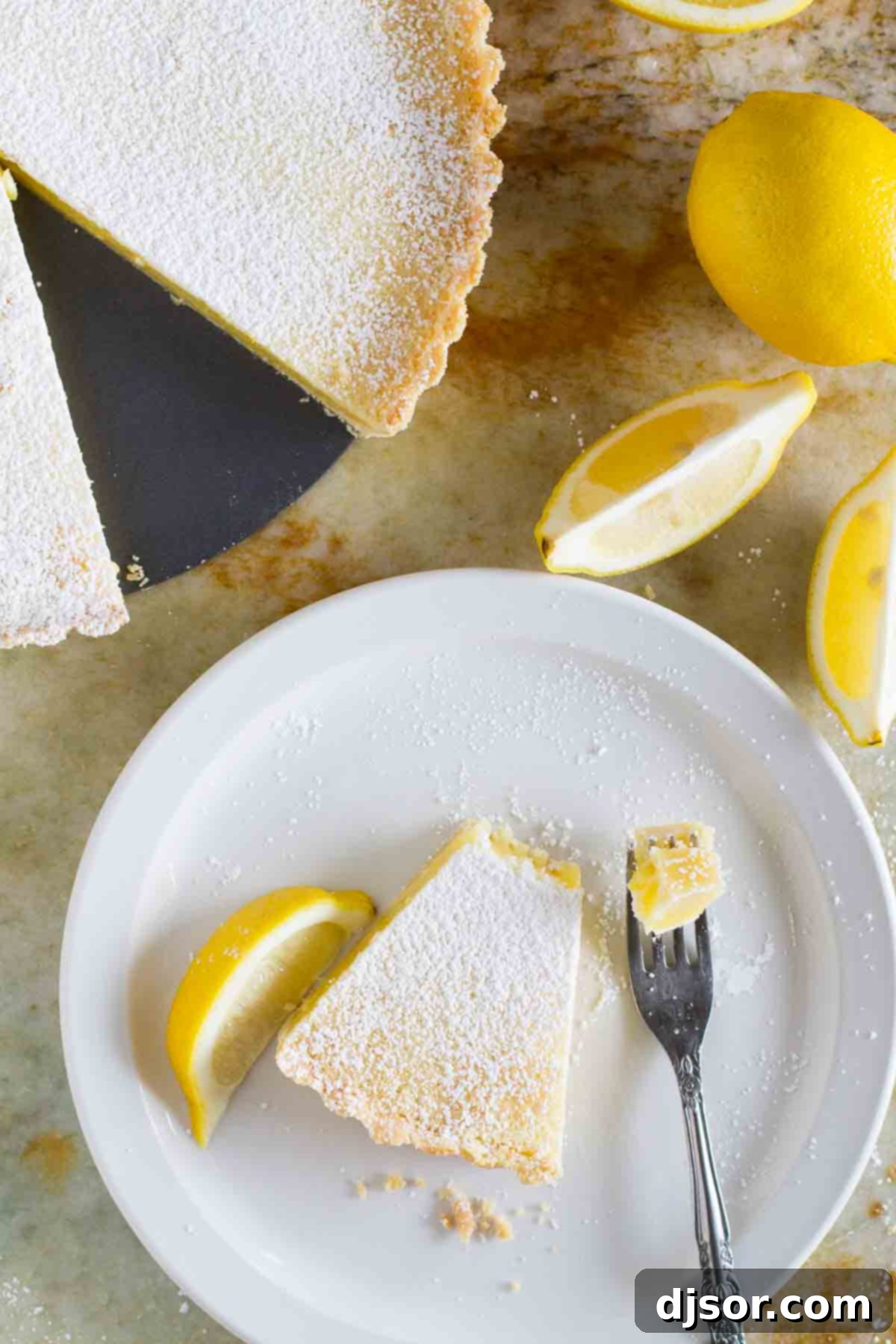 An overhead shot of a single slice of Shortbread Lemon Tart, with a fork holding a bite, highlighting its rich filling and perfect crust texture.