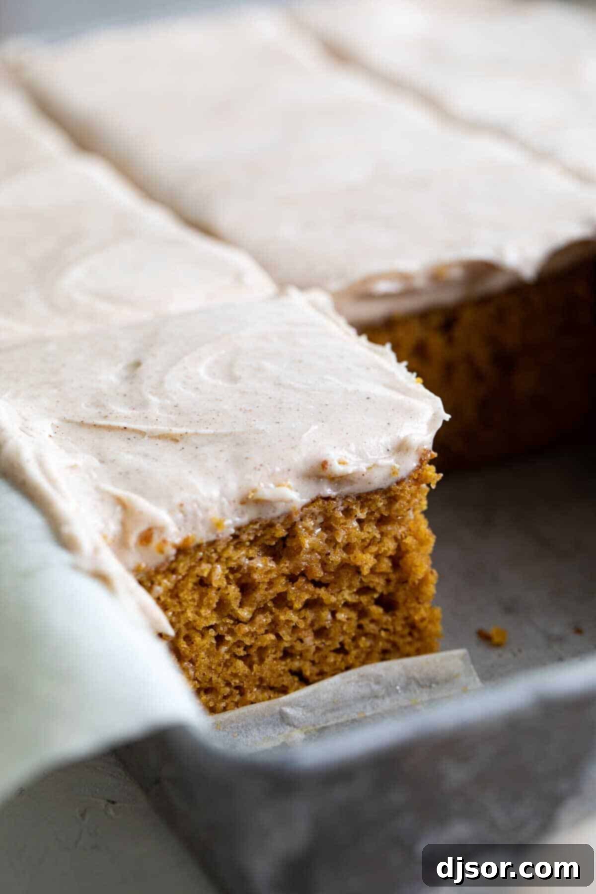 Close-up of pumpkin cake slices in a cake pan, generously topped with cinnamon cream cheese frosting.