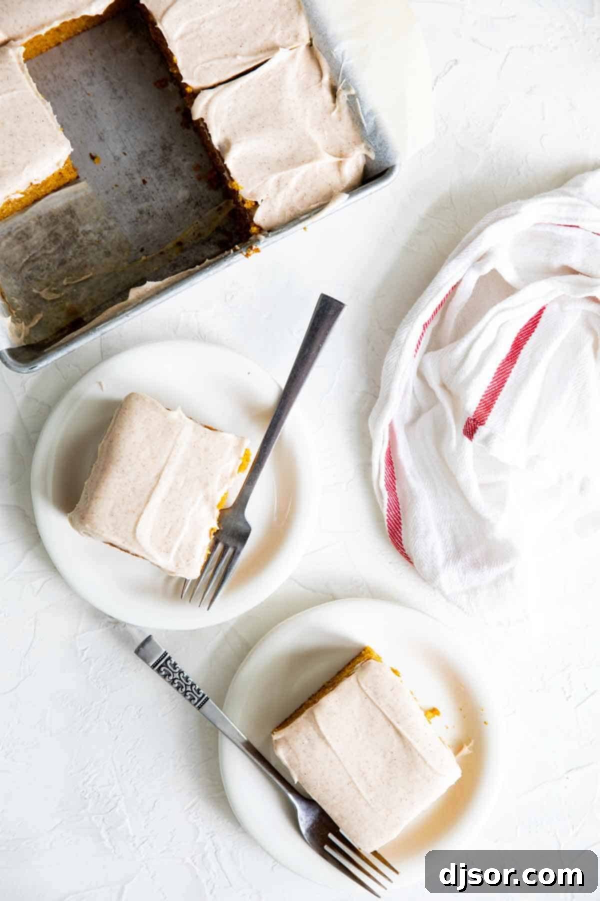 Two generous slices of pumpkin cake on individual plates, with the remaining cake in its pan in the blurred background.